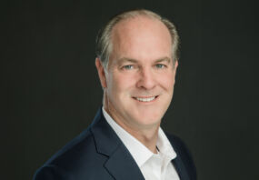 Headshot of Alex Darden in dark blazer and white shirt against dark background.