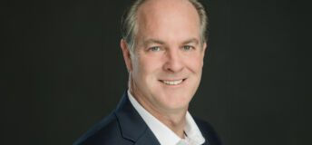 Headshot of Alex Darden in dark blazer and white shirt against dark background.