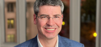 Headshot of Jay Scanlan in blue blazer and office buildings behind